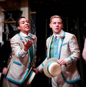 Viola with her right hand held out and hat in left hand, Sebastian holding his hat in left hand and his right hand on her hat-holding hand, both wearing gray suits with turquoise trim and vests.