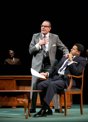 LBJ in gray suit with one hand to his chest and the other on the shoulder of MLK in blue suit sitting in chair