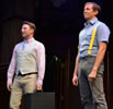 Valentine in pink oxford shirt, blue tie, tan vest and tan jeans holding a black suitcase in his left hand, Proteus in blue work shirt, gray jeans, and yellow suspenders